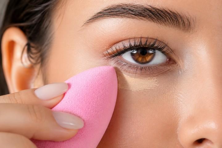 Pointed makeup sponge blending concealer under the eyes