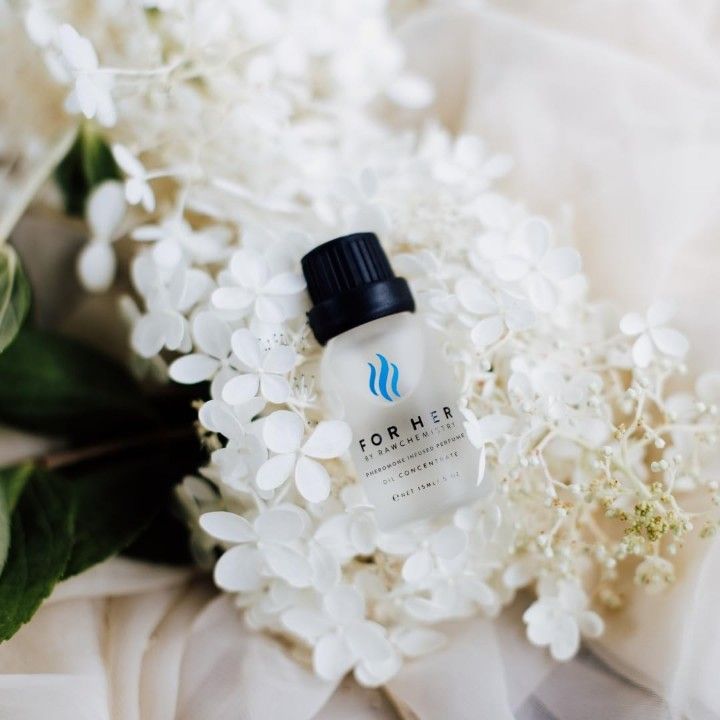 RawChemistry Pheromone Infused Women's Perfume Oil (0.5 oz) displayed on soft white flowers, showcasing the elegant bottle and premium fragrance packaging.